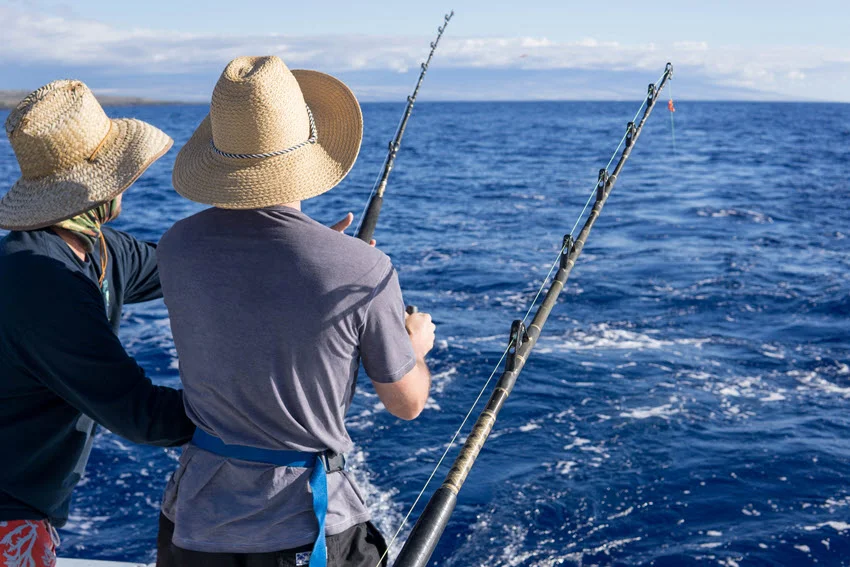 Two anglers working fishing rods from a boat while searching open blue water for fast-moving Spanish Mackerel.