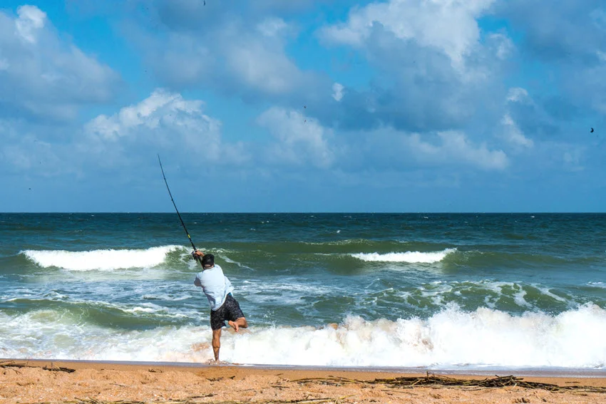 Action shot of an angler surf casting into breaking waves while targeting Spanish Mackerel from an open sandy beach.