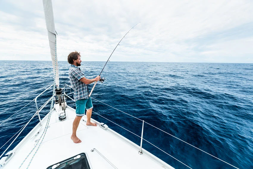 Angler standing on a boat casting a rod over deep blue offshore waters under a clear sky.