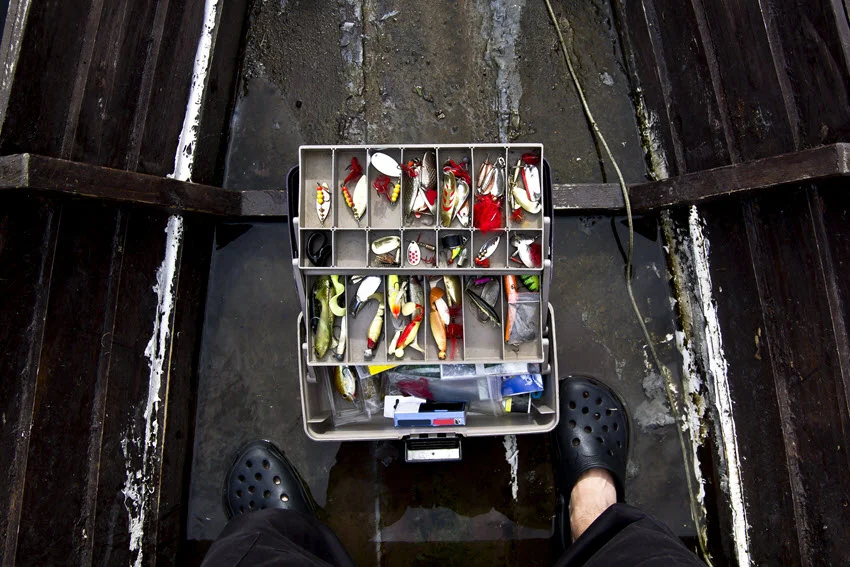 Top view of a tackle box filled with colorful lures neatly arranged on a wooden dock.
