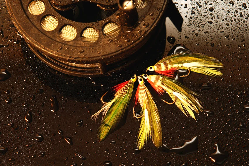 Tarpon fly lures beside a fishing reel, showing colorful baitfish patterns used for sight casting.