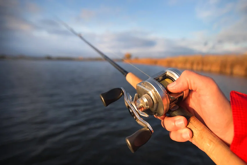 Focused shot of an angler's hand holding a wooden trolling fishing rod against a calm river landscape.