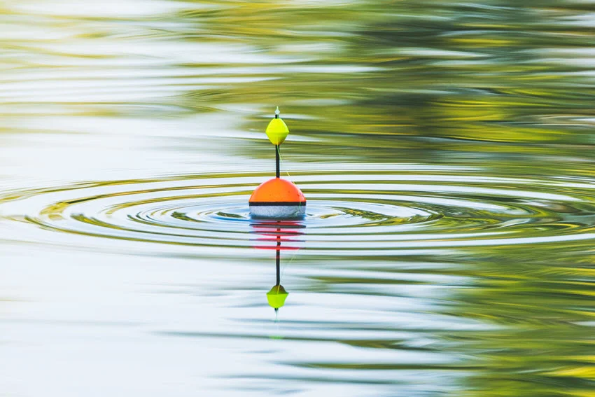 A fishing float floats on the water of the lake making circles in the water.