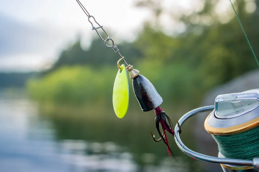 A spinning lure on a fishing reel, with the lake water in the blurry background.