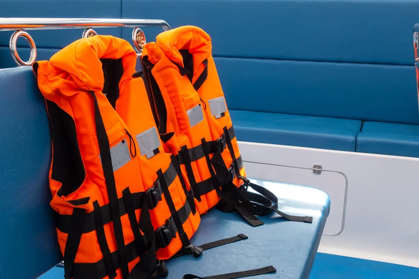 Two large orange life saving jackets placed upright on two blue benches, on a fishing boat.
