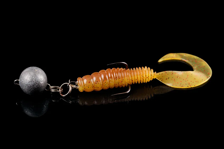 Soft fishing bait, silicone grub, with double hook and lead sinker, isolated on black background.