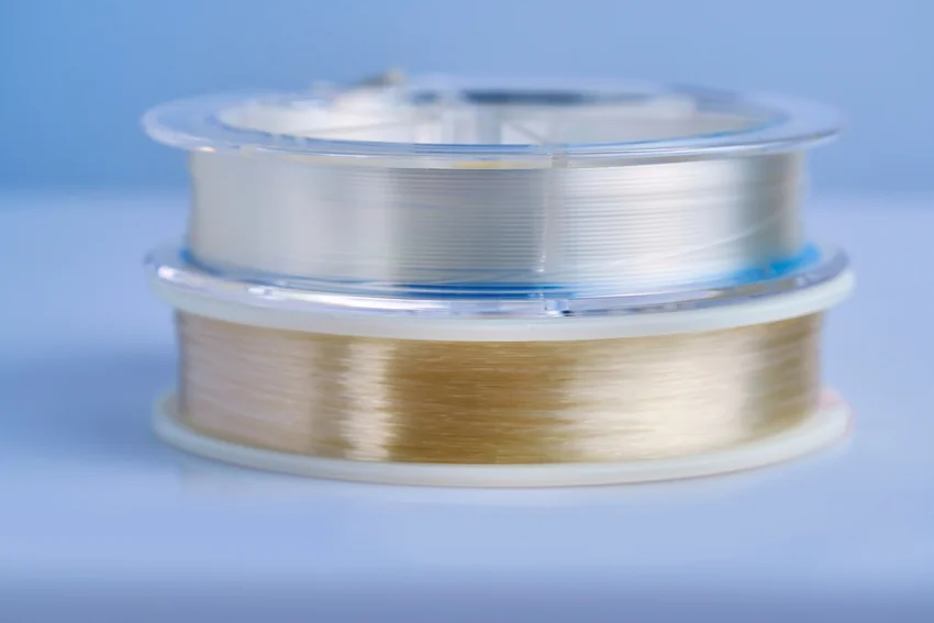 Two stacked fishing line spools containing clear and golden line, shown against a blue background with the upper spool in soft focus.