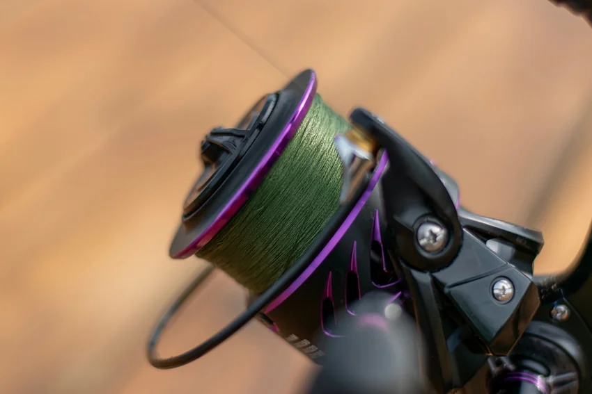 Close-up of green fishing line wound around a spinning reel spool, with the reel body and bail arm visible against a blurred background.