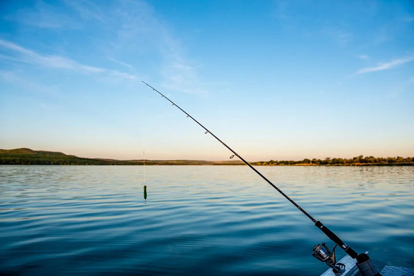 Angler holding a spinning rod on a calm lake from a small boat at sunrise.
