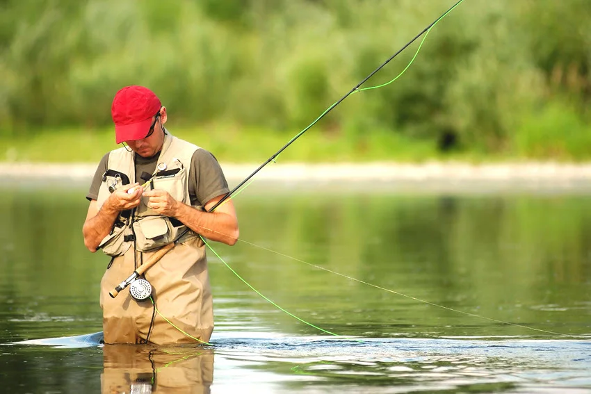 An angler preparing gear by the river, carefully setting up a fishing rod and tackle with calm water and natural surroundings creating a peaceful scene.