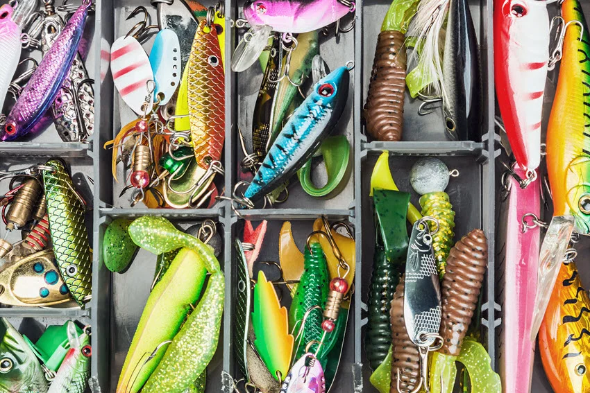 A tackle box filled with various fishing lures and accessories, neatly organized and ready for the next fishing trip. The background provides depth, emphasizing the variety of gear.