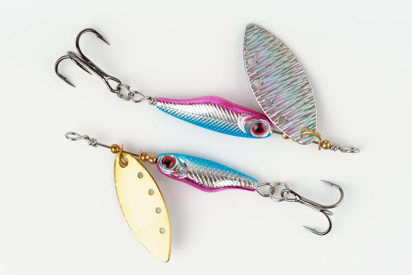 Two spinner lures for predator fishing displayed on a bright gray surface. These metal lures are designed to create vibration and flash, attracting predatory fish.