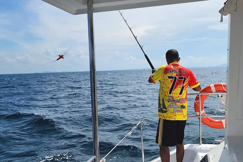 Back shot of an angler standing on a boat, preparing a rod for trolling with open water stretching out ahead.