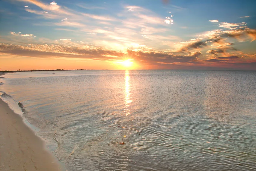 View from the shore of a sunset over the beach on Horn Island, with golden light casting across the sand and gentle waves.