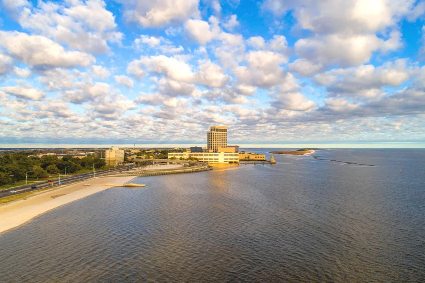 Aerial panoramic view of the Biloxi waterfront, showcasing the coastline, city buildings, and surrounding waters under clear skies.