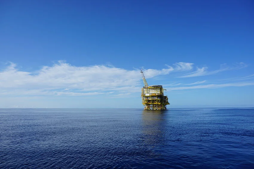 Distant view of an old oil rig standing in the middle of the Gulf of Mexico, with its weathered structure rising above the open ocean.