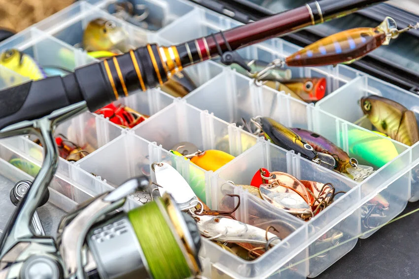 Open tackle box with metal spoons and hard-bodied lures beside a spinning reel, serving as a general illustration for the Black Drum lure discussion.