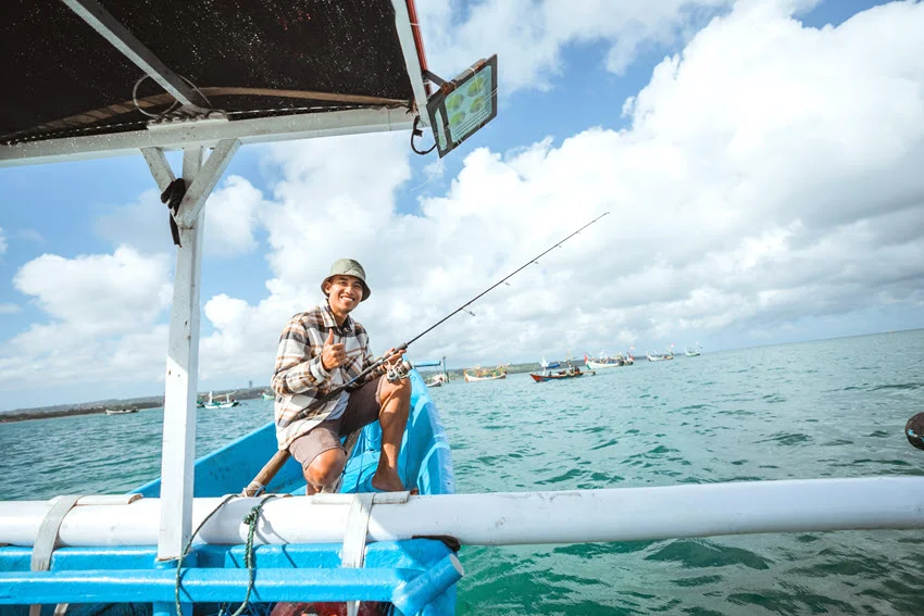 Angler holding a spinning rod aboard a small outrigger boat, illustrating the boat-based setting of drift fishing, with other vessels in the background.