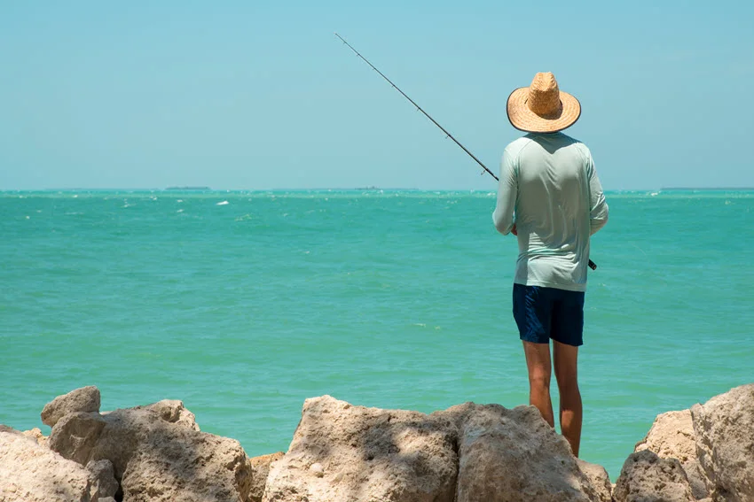 Angler fishing from rocks in Key West, Florida, illustrating a coastal setting for popping-cork fishing, with turquoise water stretching beyond.