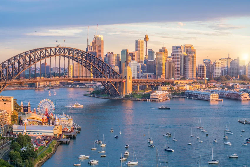Aerial view of downtown Sydney skyline in Australia during twilight, with city lights beginning to glow and the iconic landmarks visible.