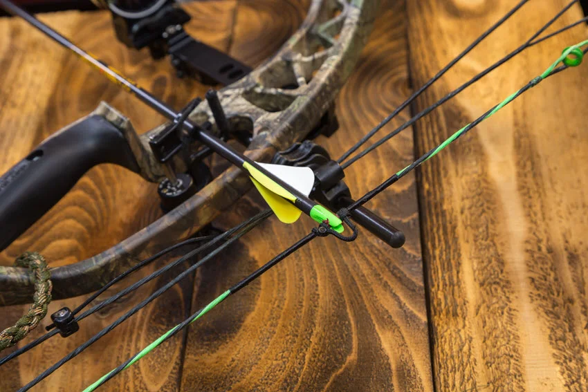 Close-up shot of a compound bow and attached arrow placed on a wooden board.