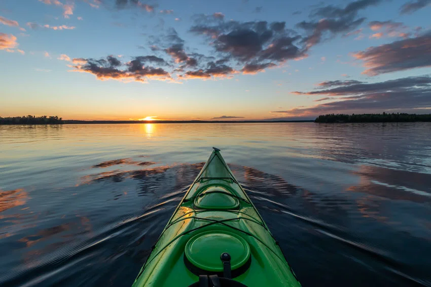 Focused view from the top of a green kayak gliding down the lake at sunset, with vibrant colors reflecting beautifully on the water.