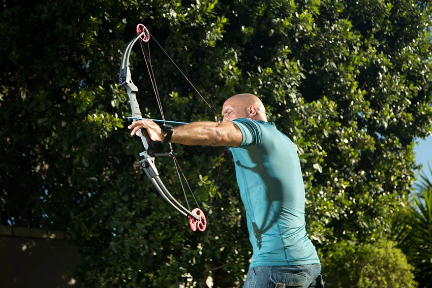 Close-up shot of a hunter standing amidst dense vegetation, holding a bow and arrow, poised and ready to strike his target.