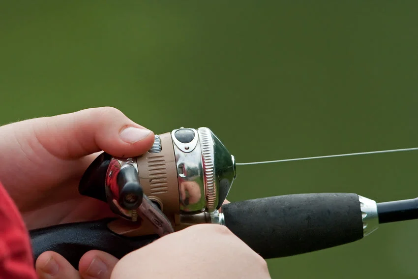 Close-up shot of spincast reels held by an angler, showcasing the reel details and grip.