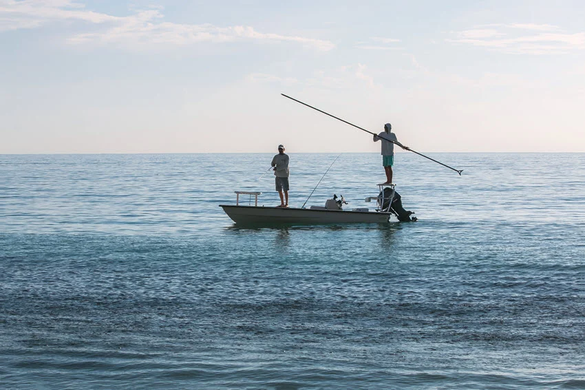A distant shot of two anglers sight fishing from a small white boat on open water, with a blurred horizon in the background.