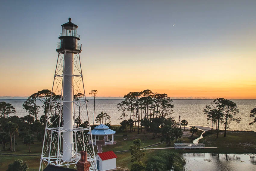 Panoramic view of Cape San Blas Lighthouse during sunset, with warm colors lighting up the sky and shoreline.