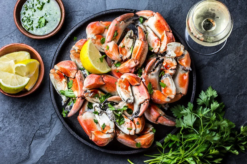 Seafood platter featuring crab tentacles on a black plate, served with white wine, lemon, and herb sauce on a slate background.