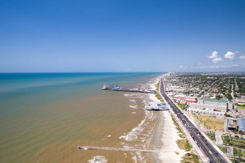 Aerial view of Galveston surf and sandy shoreline with clear green water.