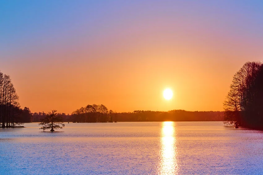 Sunset over a calm Florida lake with open water, shoreline trees, and low-light conditions often used for productive Crappie fishing.