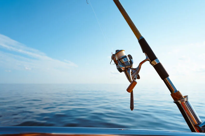 Close-up of a fishing rod on a sailboat, with the open sea in the background under a sunny sky.