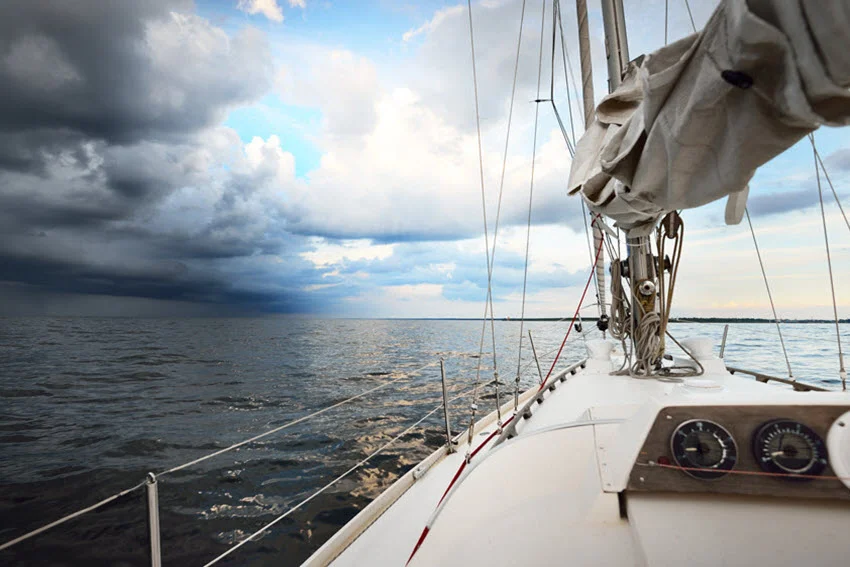 White yacht sailing in the open sea at sunset, with dramatic sky and colorful clouds after a storm.