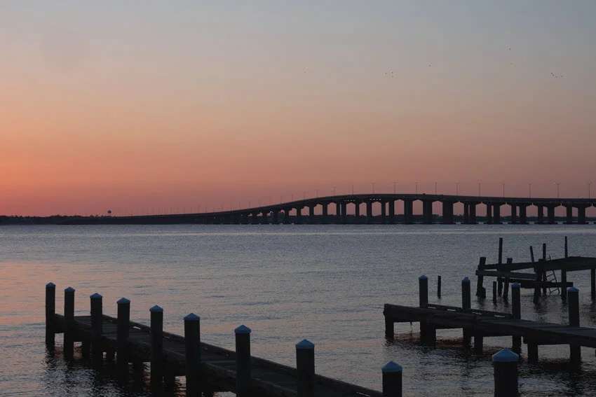 Wooden piers and jetties in Bay St. Louis, Mississippi, with the arched bridge stretching over the bay in the background.