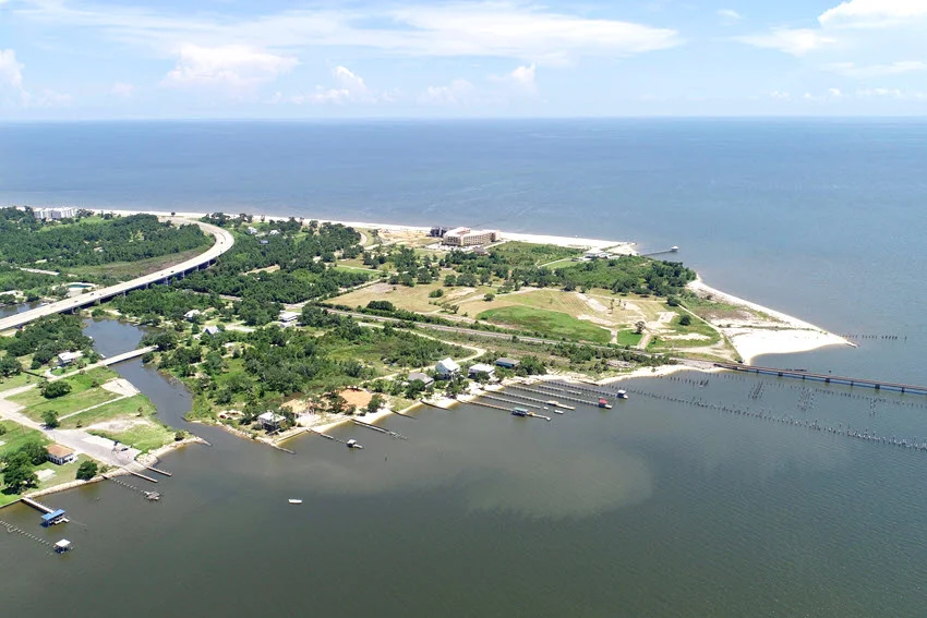 Aerial view of Bay St. Louis, Mississippi, showing the coastline, bridge, and fishing piers extending into calm Gulf waters on a clear day.