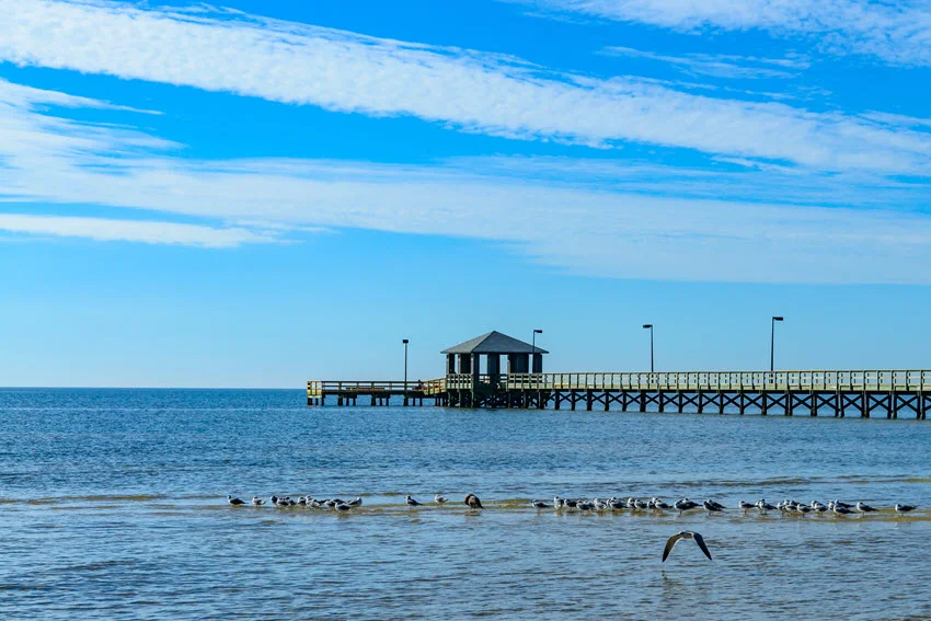 View of Dunbar Avenue Pier in Bay St. Louis, Mississippi, stretching over calm waters at sunset with a covered shelter at the end.