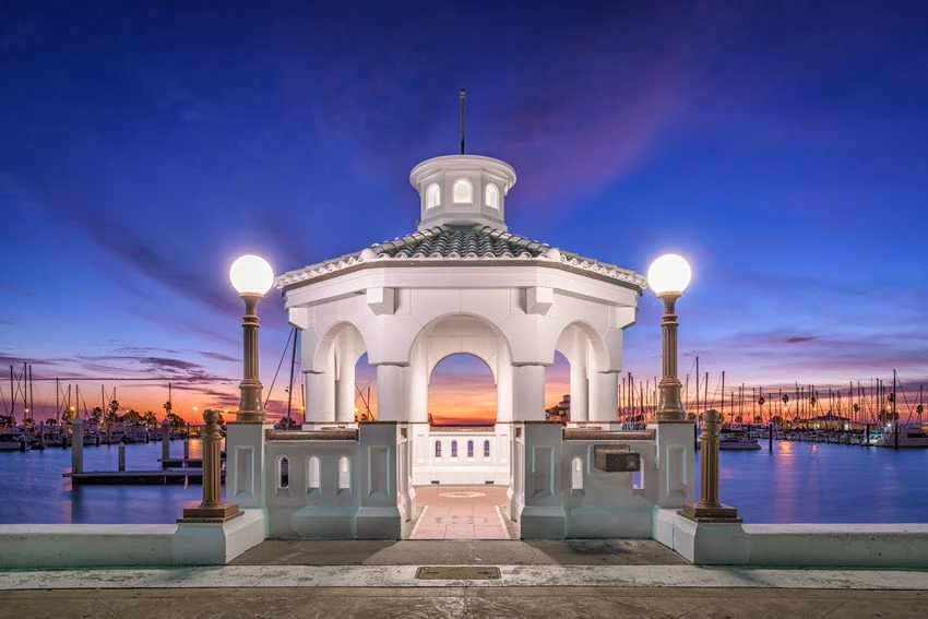View of Corpus Christi, Texas, USA, on the seawall at dawn, with the first light of day casting a soft glow over the waterfront. The calm waters reflect the pastel hues of the morning sky, creating a serene and picturesque coastal scene.