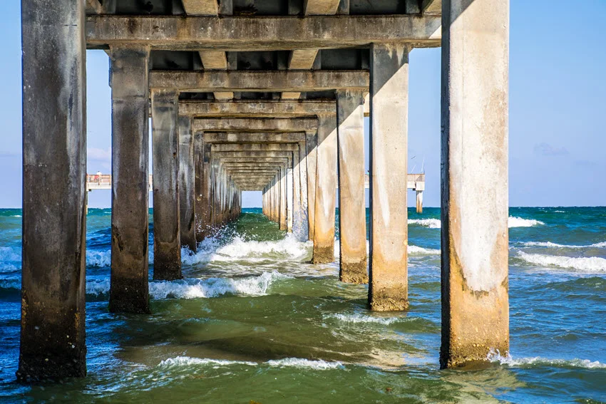 Fishing pier extending into the ocean in Corpus Christi, Texas, offering a scenic spot for anglers and visitors. The wooden structure stretches over the Gulf of Mexico, with waves rolling beneath and a vast coastal horizon in the background.