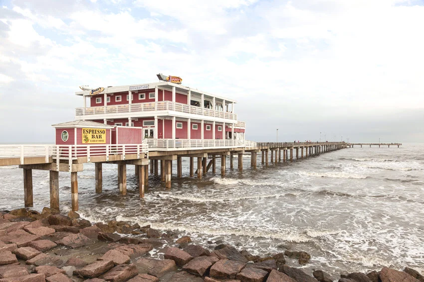 Fishing and leisure pier on the Gulf of Mexico coast in Galveston Island, Texas, USA. The wooden pier extends over the water, offering a scenic spot for anglers and visitors to enjoy the coastal breeze and ocean views.