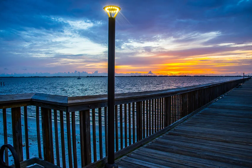 A serene fishing pier in Jensen Beach, Florida, illuminated by artificial lights blending with early dawn light, creating a peaceful and captivating atmosphere.