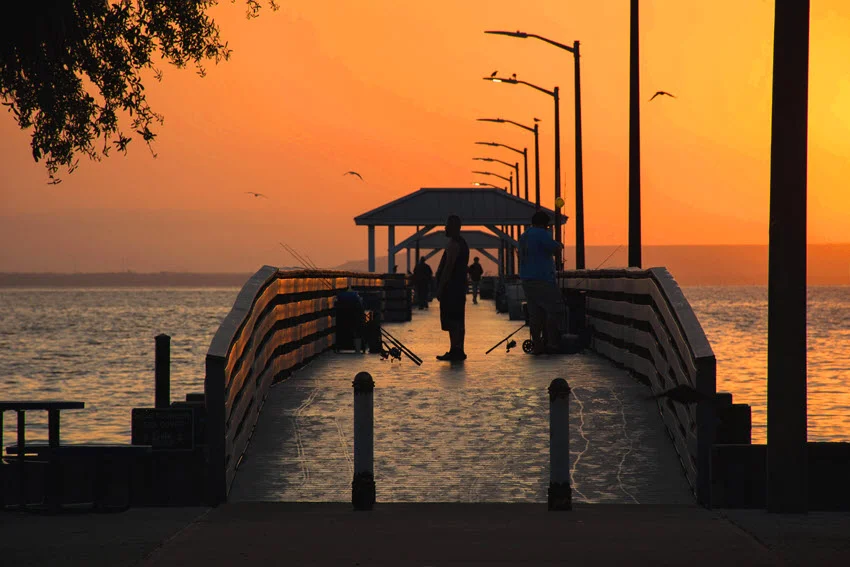 Sunrise at the pier in Jensen Beach, Florida, with early morning light casting a warm glow over calm waters and the pier silhouetted against vibrant colors of the rising sun.