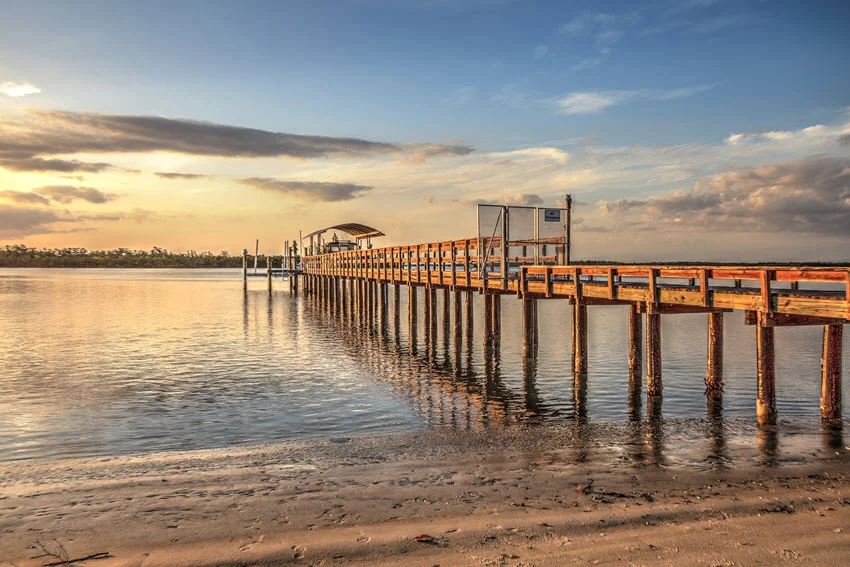 View of the Isle of Capri Fire Department pier for Boat 90 at sunset, near Marco Island, Florida, USA. The scene features the pier bathed in the warm hues of the setting sun, creating a serene and picturesque backdrop suitable for editorial use.