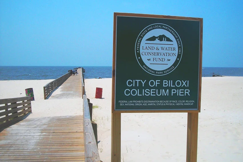 The Coliseum Pier, stretching into the Gulf of Mexico, located across from the Mississippi Coast Coliseum. The wooden pier extends over calm waters, offering a scenic coastal view with the coliseum in the background.