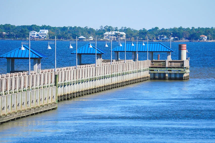 A pier extending into the bay at Bay St. Louis, Mississippi, within the marina. Calm waters reflect the sky, creating a peaceful coastal scene with boats docked nearby.