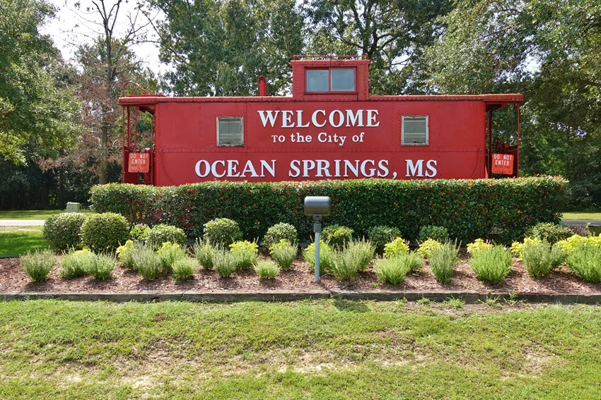 A red welcome sign displayed on an old train marking the entrance to the city of Ocean Springs, Mississippi.
