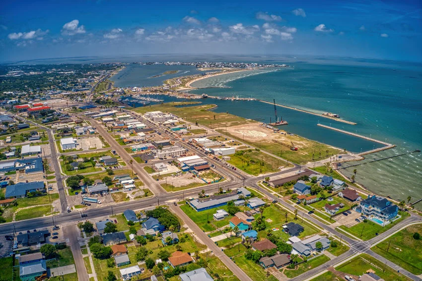 Aerial view of the coastal town of Rockport, Texas, situated along the Gulf of Mexico. The scenic landscape showcases the town's waterfront, marinas, and sandy shores, highlighting its charm as a popular fishing and boating destination.