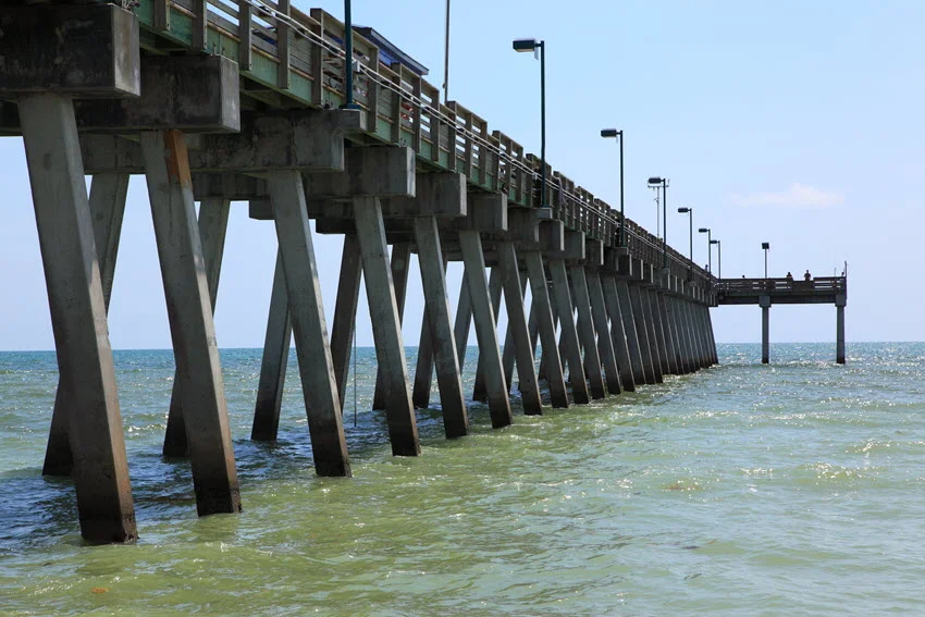 Public fishing pier in Sarasota, Florida, stretching over calm Gulf waters with anglers along the rail and a sunny coastal view in the background.