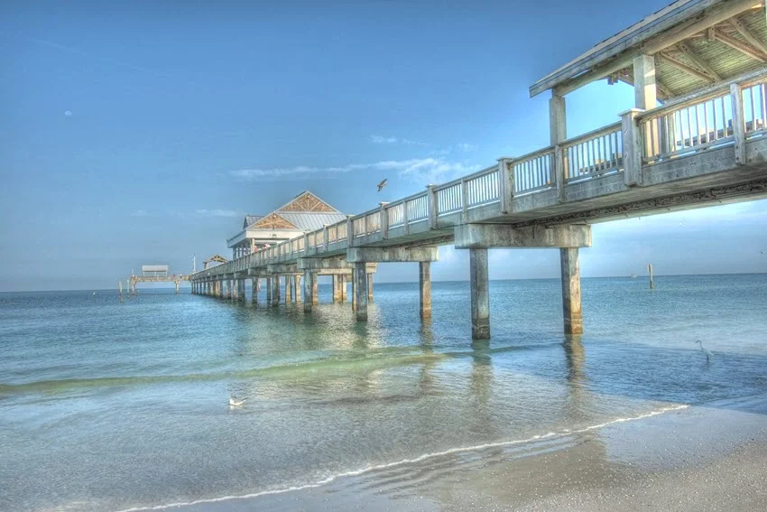 ngler fishing at a pier in Florida, USA. The scene captures the peaceful setting of the coastline, with clear skies and calm waters, offering an ideal environment for fishing.